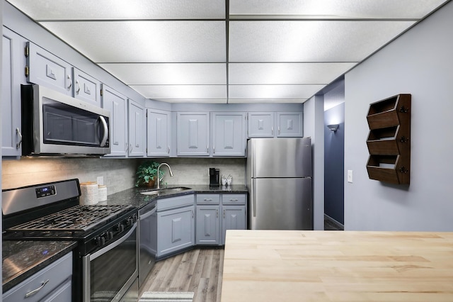 kitchen with light wood-style flooring, a sink, appliances with stainless steel finishes, gray cabinets, and decorative backsplash