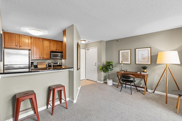 kitchen featuring a kitchen bar, light carpet, dark countertops, appliances with stainless steel finishes, and brown cabinetry