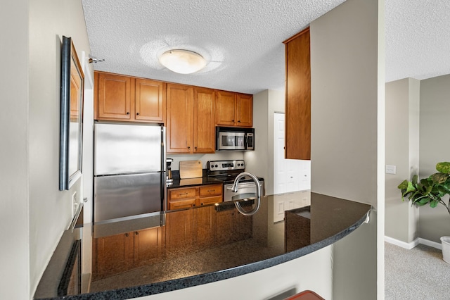 kitchen with dark stone countertops, brown cabinetry, baseboards, a peninsula, and appliances with stainless steel finishes