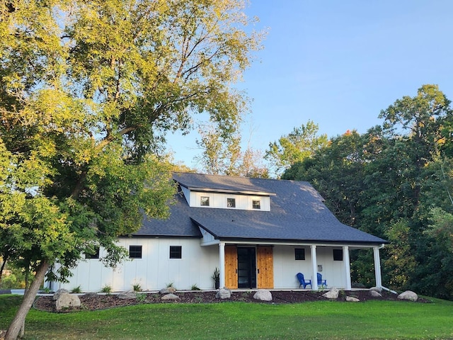 modern farmhouse style home with roof with shingles, a porch, board and batten siding, and a front yard