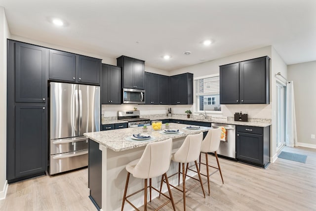 kitchen featuring stainless steel appliances, a sink, light stone countertops, light wood-type flooring, and a kitchen bar