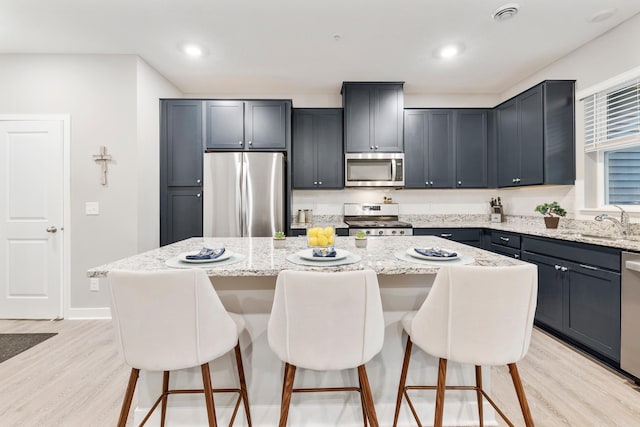 kitchen with light wood-style flooring, a kitchen bar, light stone counters, and stainless steel appliances