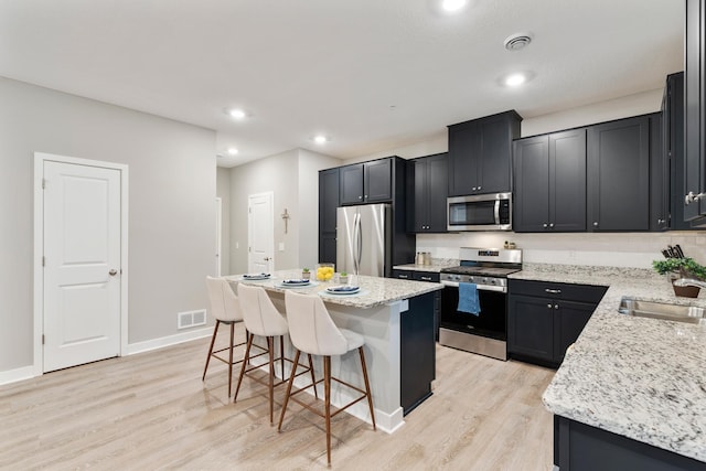 kitchen featuring a breakfast bar, stainless steel appliances, visible vents, light wood-style flooring, and a sink