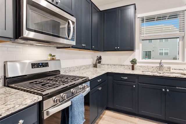 kitchen with light wood finished floors, tasteful backsplash, light stone countertops, stainless steel appliances, and a sink