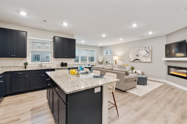 kitchen featuring a glass covered fireplace, open floor plan, a center island, and light wood finished floors