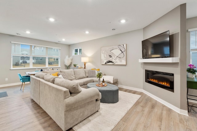 living area with baseboards, a glass covered fireplace, light wood-style flooring, and recessed lighting