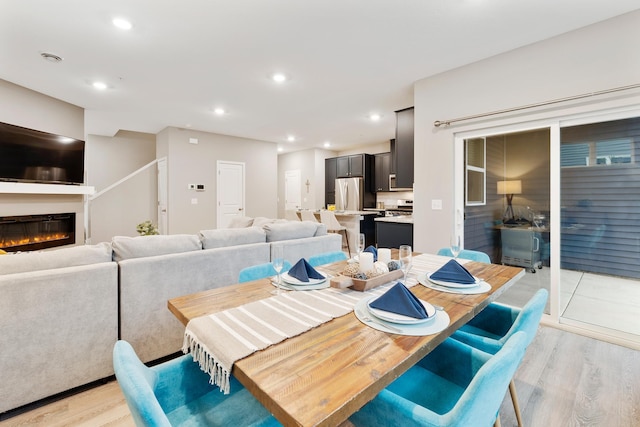 dining space with light wood-type flooring, a glass covered fireplace, and recessed lighting