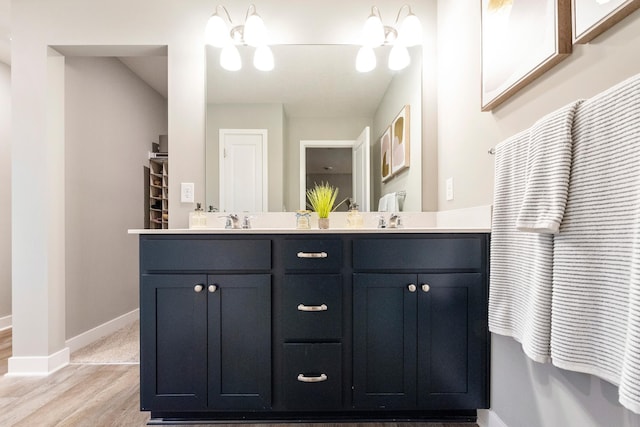 full bath featuring a sink, double vanity, wood finished floors, and baseboards