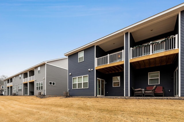 rear view of house with a balcony, a lawn, and central AC