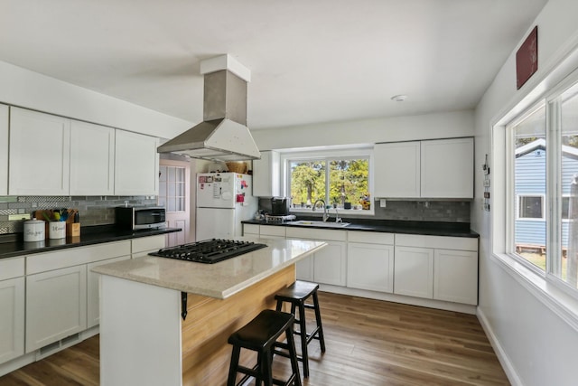 kitchen with island exhaust hood, black gas cooktop, stainless steel microwave, freestanding refrigerator, and a sink