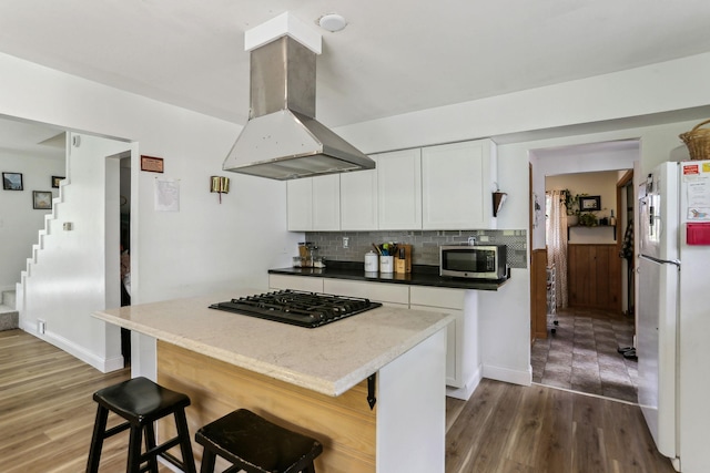 kitchen with island exhaust hood, black gas cooktop, stainless steel microwave, backsplash, and freestanding refrigerator