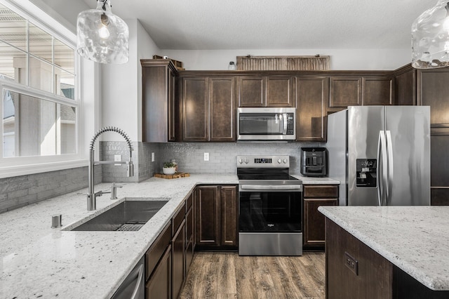 kitchen featuring dark brown cabinetry, stainless steel appliances, wood finished floors, a sink, and tasteful backsplash