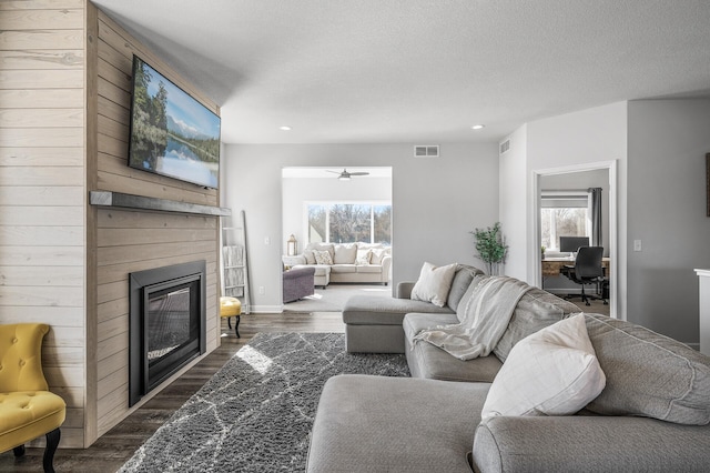 living area featuring a glass covered fireplace, dark wood-style flooring, visible vents, and plenty of natural light