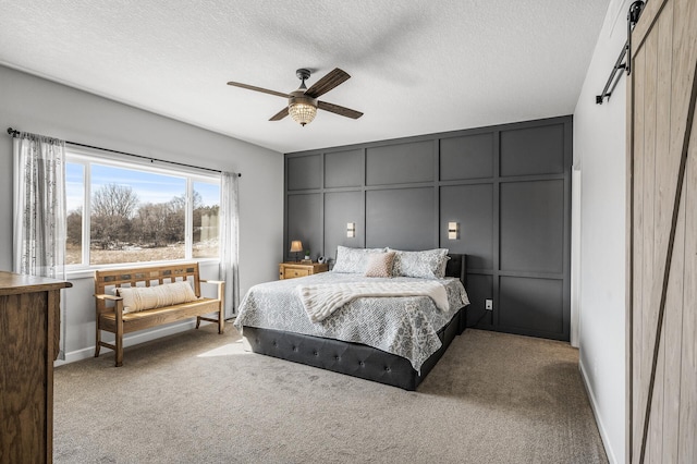 bedroom featuring a barn door, a ceiling fan, a textured ceiling, carpet floors, and a decorative wall