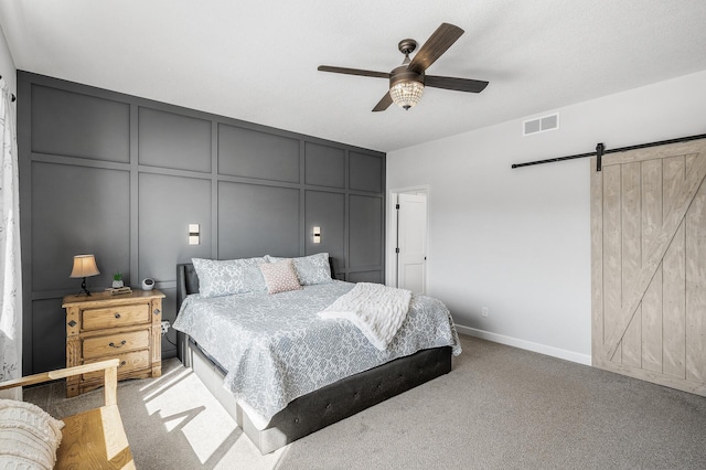 carpeted bedroom featuring ceiling fan, a barn door, visible vents, and a decorative wall