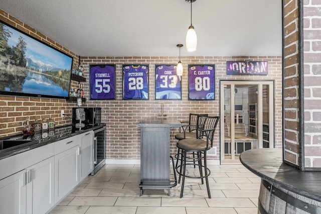 bar featuring beverage cooler, brick wall, hanging light fixtures, and a community bar