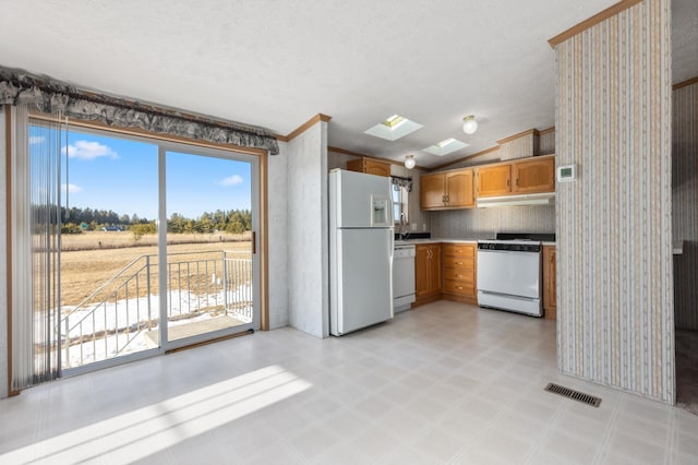 kitchen with vaulted ceiling with skylight, white appliances, a sink, visible vents, and light floors