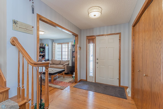 entryway featuring a textured ceiling, stairway, light wood-style flooring, and baseboards