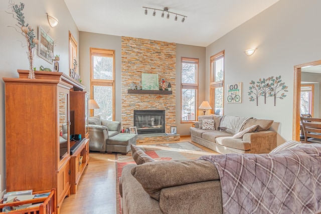 living area featuring light wood finished floors, track lighting, and a stone fireplace