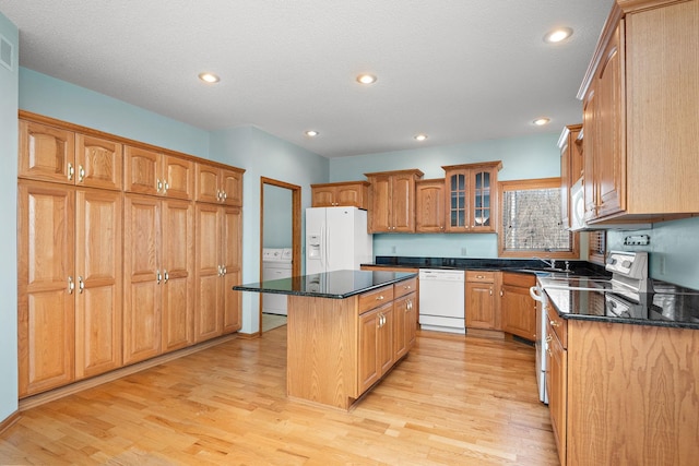 kitchen featuring white appliances, glass insert cabinets, washer / clothes dryer, a center island, and light wood-style floors