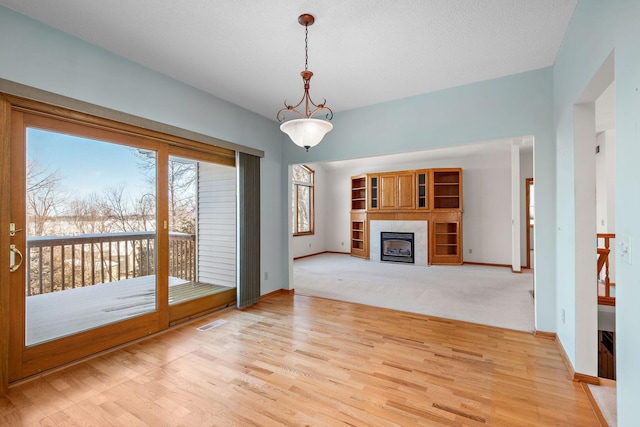 unfurnished living room with a textured ceiling, a tile fireplace, light wood-style flooring, visible vents, and baseboards