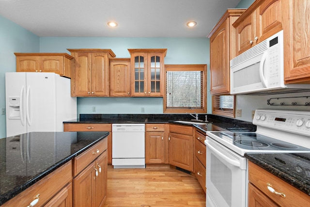 kitchen featuring white appliances, dark stone counters, light wood-style flooring, glass insert cabinets, and a sink