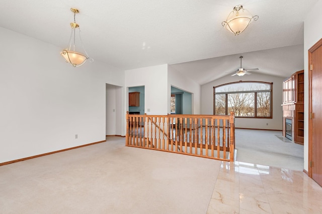 unfurnished room with baseboards, vaulted ceiling, a glass covered fireplace, and light colored carpet