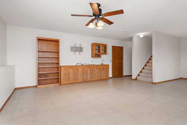 unfurnished living room with stairs, built in shelves, a ceiling fan, and baseboards