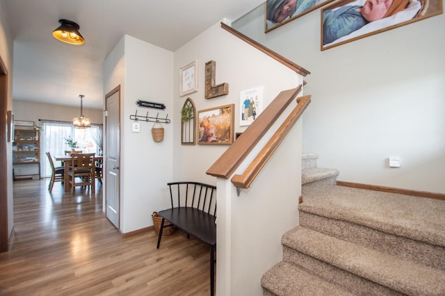 stairway with baseboards, wood finished floors, and a notable chandelier
