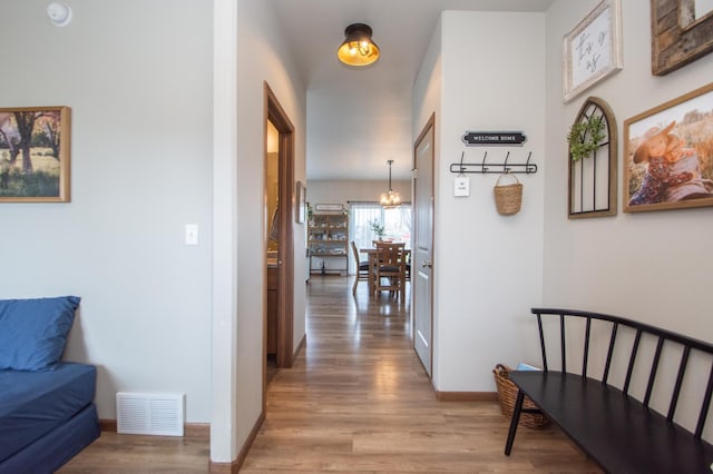 hallway with baseboards, visible vents, a chandelier, and light wood finished floors