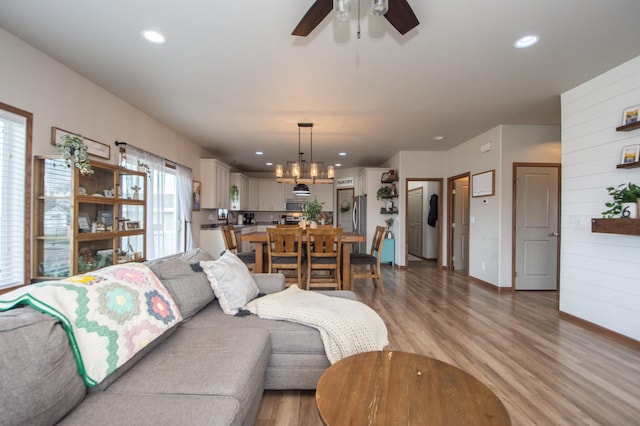 living room featuring light wood-style floors, baseboards, recessed lighting, and ceiling fan with notable chandelier
