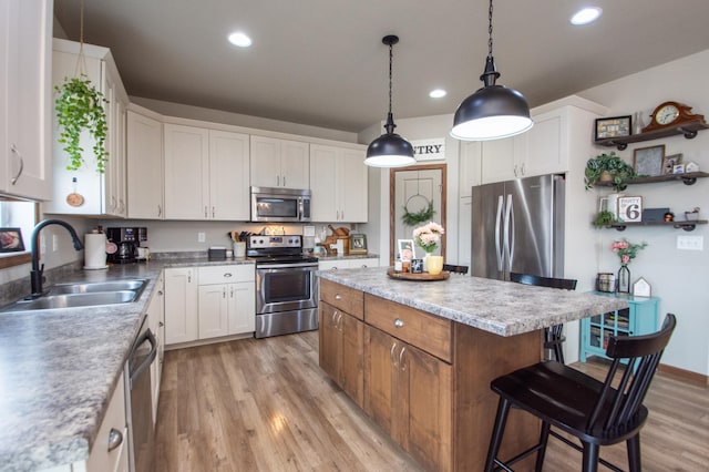 kitchen with stainless steel appliances, a kitchen island, a sink, white cabinetry, and light wood-type flooring