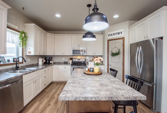 kitchen featuring a sink, stainless steel appliances, a kitchen bar, light wood-style flooring, and white cabinetry