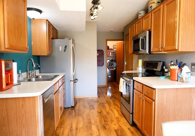 kitchen with washer / clothes dryer, stainless steel appliances, a textured ceiling, light wood-type flooring, and a sink