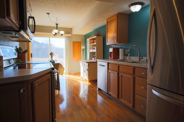 kitchen with stainless steel appliances, brown cabinetry, a sink, and dark wood-style floors