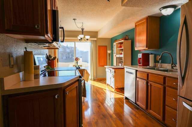 kitchen with a notable chandelier, stainless steel appliances, wood finished floors, a sink, and pendant lighting