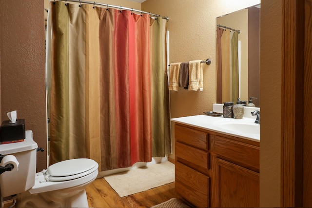 full bathroom featuring a textured wall, vanity, toilet, and wood finished floors