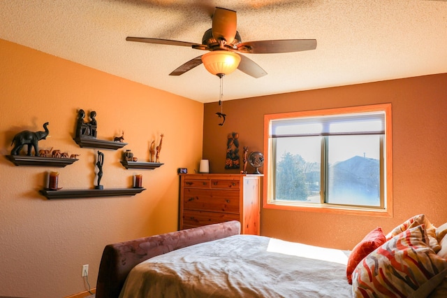 bedroom featuring a ceiling fan, a textured wall, and a textured ceiling