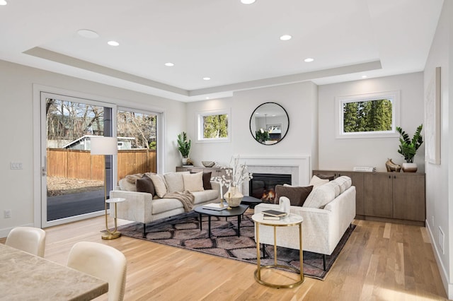 living room featuring a tray ceiling, light wood-style flooring, recessed lighting, and a high end fireplace