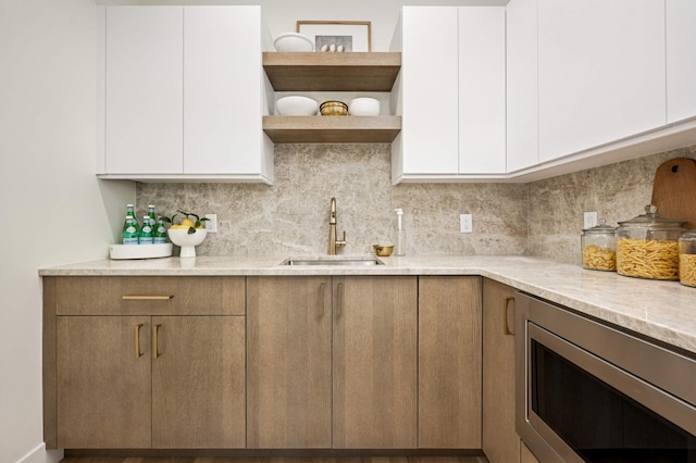 kitchen with white cabinetry, stainless steel microwave, tasteful backsplash, and a sink