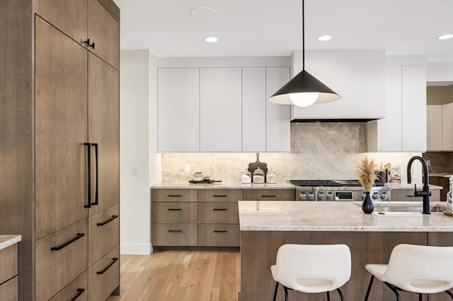 kitchen with light wood-type flooring, modern cabinets, a sink, light stone counters, and a kitchen breakfast bar