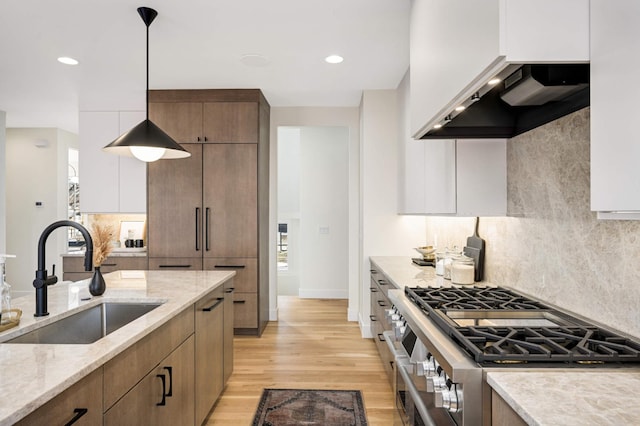 kitchen with light wood finished floors, tasteful backsplash, double oven range, light stone counters, and a sink