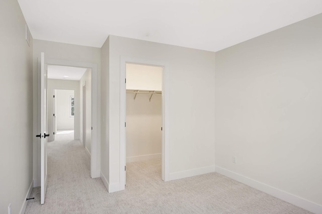 unfurnished bedroom featuring baseboards, light carpet, a closet, and a spacious closet