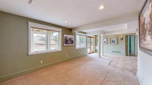 spare room featuring light carpet, decorative columns, visible vents, and a textured ceiling