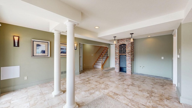 unfurnished living room featuring stairs, a fireplace, baseboards, and ornate columns