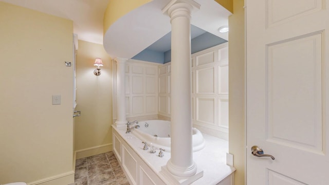 full bath featuring baseboards, decorative columns, and a whirlpool tub