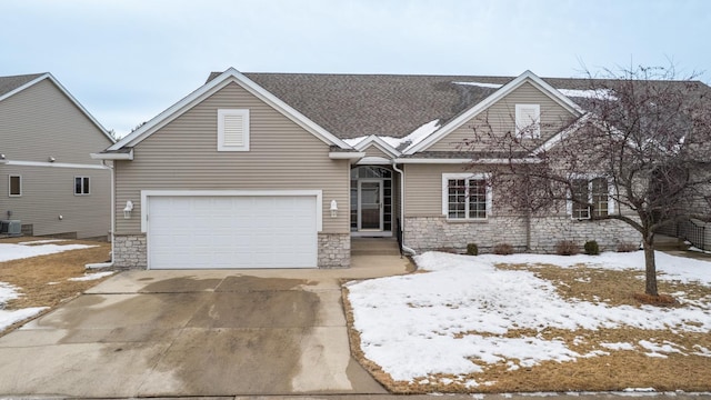 view of front of home with roof with shingles, central AC unit, a garage, stone siding, and driveway