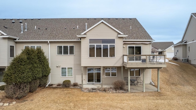 rear view of property featuring cooling unit, roof with shingles, a patio, and a lawn