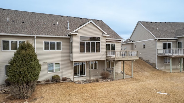 back of property featuring a lawn, a patio, a wooden deck, and a shingled roof