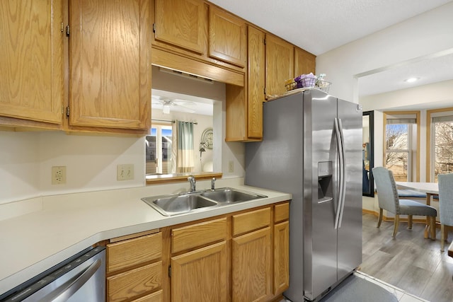 kitchen with light wood-style flooring, stainless steel appliances, a sink, light countertops, and brown cabinetry